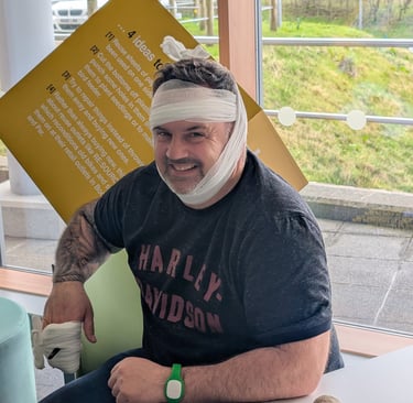 Smiling man with head bandage and hand dressing sitting in a hospital waiting room.