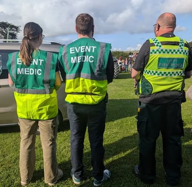 Three event medic first aid responders wearing high-visibility green vests standing in a field.