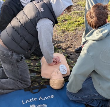 Students practicing outdoor CPR training using a Little Anne medical mannequin and AED pads.