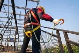 Construction worker wearing a safety harness and fall protection lanyard at a high-elevation site.