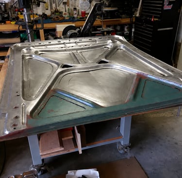A custom steel car hood restoration project on a metal workbench in a professional garage.