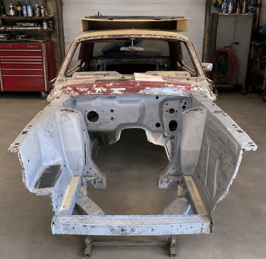 A vintage classic car frame undergoing restoration in an auto body repair shop.