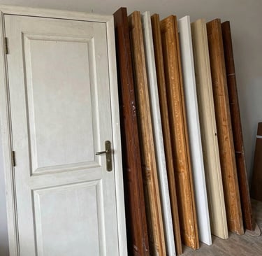 A collection of reclaimed wooden interior doors in various finishes leaning against a white wall.