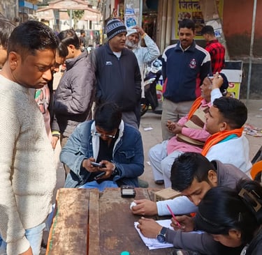 A crowded outdoor information booth in India with people gathering at a desk to complete official forms.