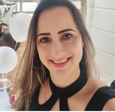 A smiling woman with long brown hair and hoop earrings poses in front of party balloons.