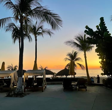 Silhouetted palm trees and beach cabanas at a tropical resort during a vibrant golden sunset.
