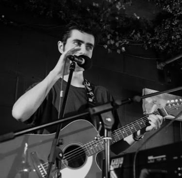 Black and white photo of Brighton musician Olly Williams singing and playing guitar