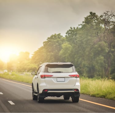 Camioneta blanca conduciendo en carretera solitaria con el sol de frente