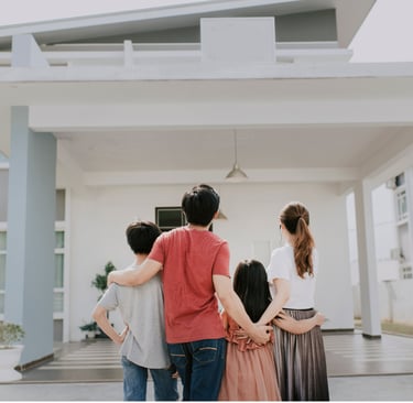 Familia abrazada contemplando su vivienda de color blanco