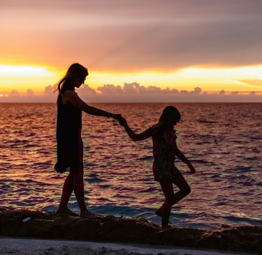Madre e hija caminando por la playa tomadas de la mano
