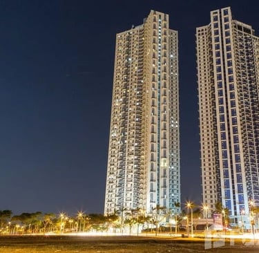 Two modern luxury high-rise residential towers illuminated against a dark night sky in a city.