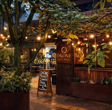 Fachada iluminada do restaurante Okone em São Paulo, destacando a área externa com mesas, luzes decorativas e paisagismo