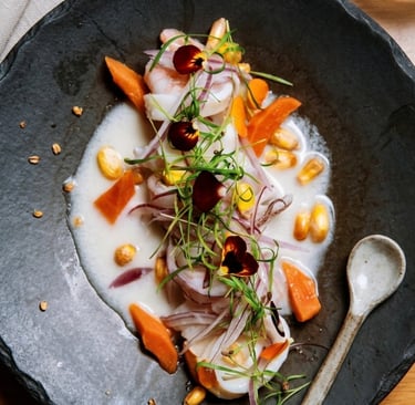 Ceviche de peixe e camarão com milho, batata-doce, cebola roxa e flores comestíveis em um prato fundo com leite de tigre.