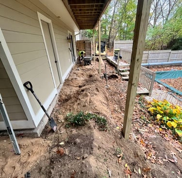 Landscaping contractors excavating dirt for a new retaining wall and drainage system under a wooden deck.