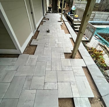 A backyard home improvement project showing light grey pavers being installed for a new stone patio.