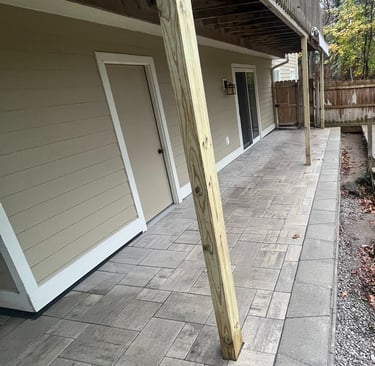 Backyard patio with grey stone pavers installed underneath a raised wooden deck.