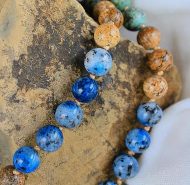 Collar mala de cuentas de gemas de cianita azul natural y jaspe, colocado sobre una piedra rústica.