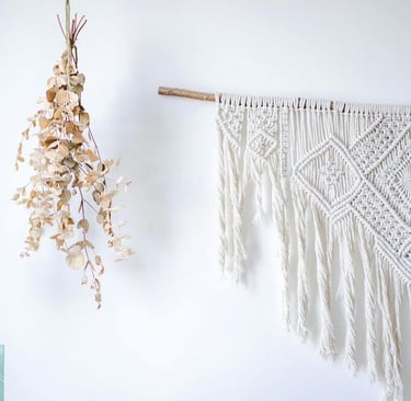 adorno artesanal hecho con macramé sobre una pared blanca y madera