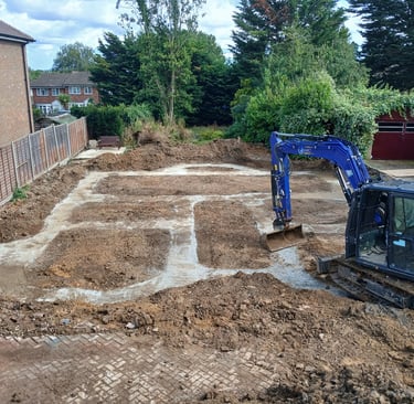 Blue excavator digging concrete footings for a new house foundation in a residential construction site.