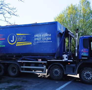 Blue JMC Groundworks and Demolition skip loader truck parked at a construction site.