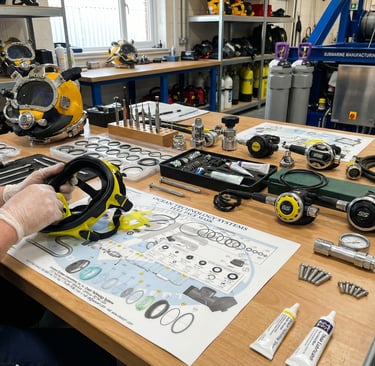 Technician in a workshop performing maintenance on a yellow diving full face mask and regulator equipment.