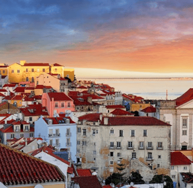 Panoramic sunset over Lisbon's Alfama district featuring red tile roofs and the National Pantheon.
