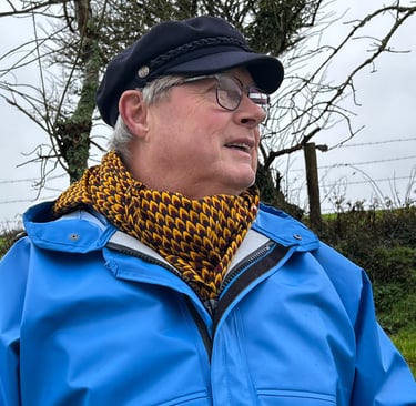 A weathered faced man with waterproof coat and captains hat wearing a noseknot bandane to keep warm