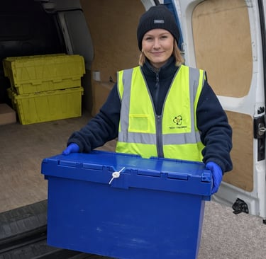 A smiling TTB Circular employee holds a security-sealed crate next to an open van.