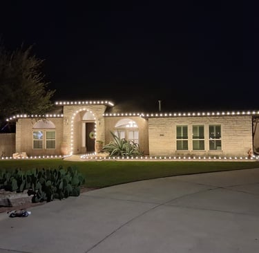 A single-story stone house at night decorated with white Christmas roofline lights in corpus christi