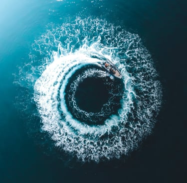 Aerial view of a motorboat creating a circular white foam wake in deep blue ocean water.
