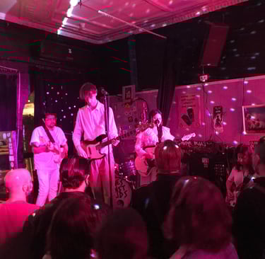 Library Siesta the band, all in white on stage playing to a packed crowd, bathed in a red light. 