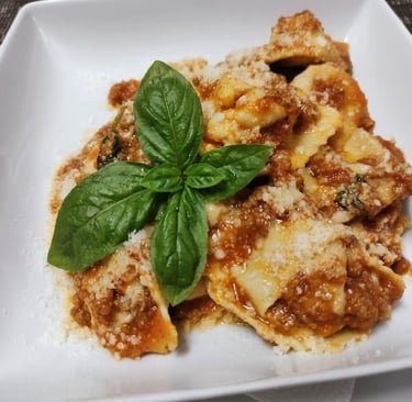 Piatto di ravioli artigianali al ragù di carne con una foglia di basilico fresco al centro.
