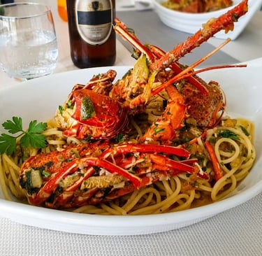 Spaghetti conditi con aragosta e pomodorini serviti in un piatto bianco di design.
