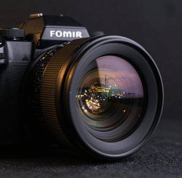 Close-up of a high-end camera lens reflecting the city lights of Istanbul at dusk. The background is a soft-focus dark slate black, with subtle metallic gold glimmers on the camera's body.