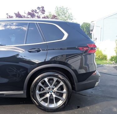 Side profile of a black BMW SUV parked on a driveway, showing the rear wheel and tail light.