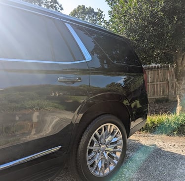 Rear profile of a black GMC Yukon SUV featuring chrome wheels and polished trim in sunlight.