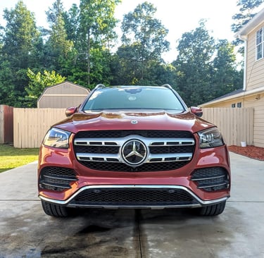Front view of a red Mercedes-Benz GLS SUV parked on a concrete driveway in front of a house.