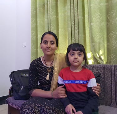 A mother and young daughter sit together on a couch in front of green curtains.