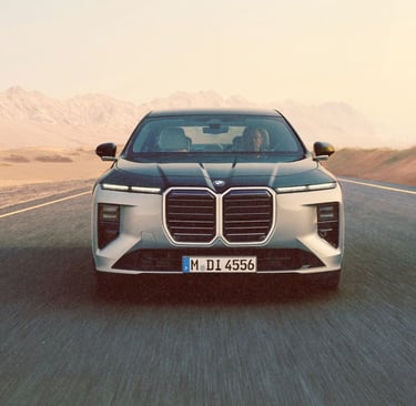 Front view of a silver BMW i7 electric luxury sedan driving on a desert road at sunset.