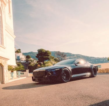 Sleek black luxury coupe parked on a sunny driveway outside a Mediterranean villa with a coastal view.