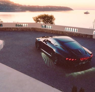 Black luxury sports car parked on a scenic coastal driveway overlooking the ocean at sunset.