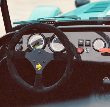 Interior view of a Caterham sports car featuring a Momo steering wheel and carbon fiber dashboard gauges.