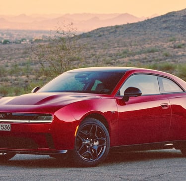 A sleek red Dodge Charger Daytona EV parked in a desert landscape during a vibrant sunset.