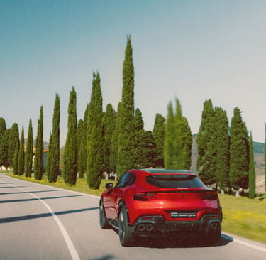A red Ferrari Purosangue SUV driving on a scenic road lined with tall cypress trees in Tuscany.
