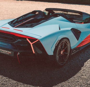 A light blue and orange Fenomeno Roadster luxury sports car parked on a gravel surface.