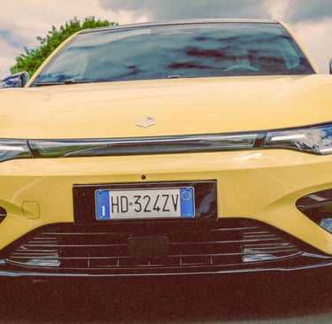 A yellow electric car driving on a scenic road with a close-up view of the front grille and headlights.