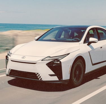 White Lexus es sedan driving on a scenic coastal highway near the ocean.