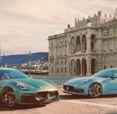 Two Maserati GranTurismo luxury sports cars parked in a historic European plaza near a grand building.