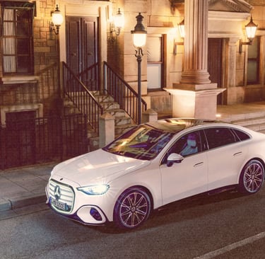 A white Mercedes-Benz electric c-class parked on a city street at night with vintage architecture.