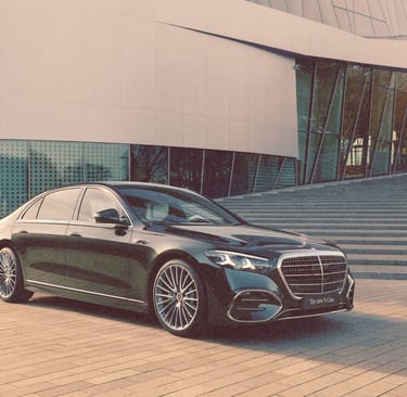 A black Mercedes-Benz S-Class luxury sedan parked in front of a modern glass building with stone steps.
